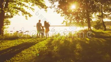 幸福的一家人走在海边。 农村的田野和树木。 日落或日出的暖色。 有爱心的父母